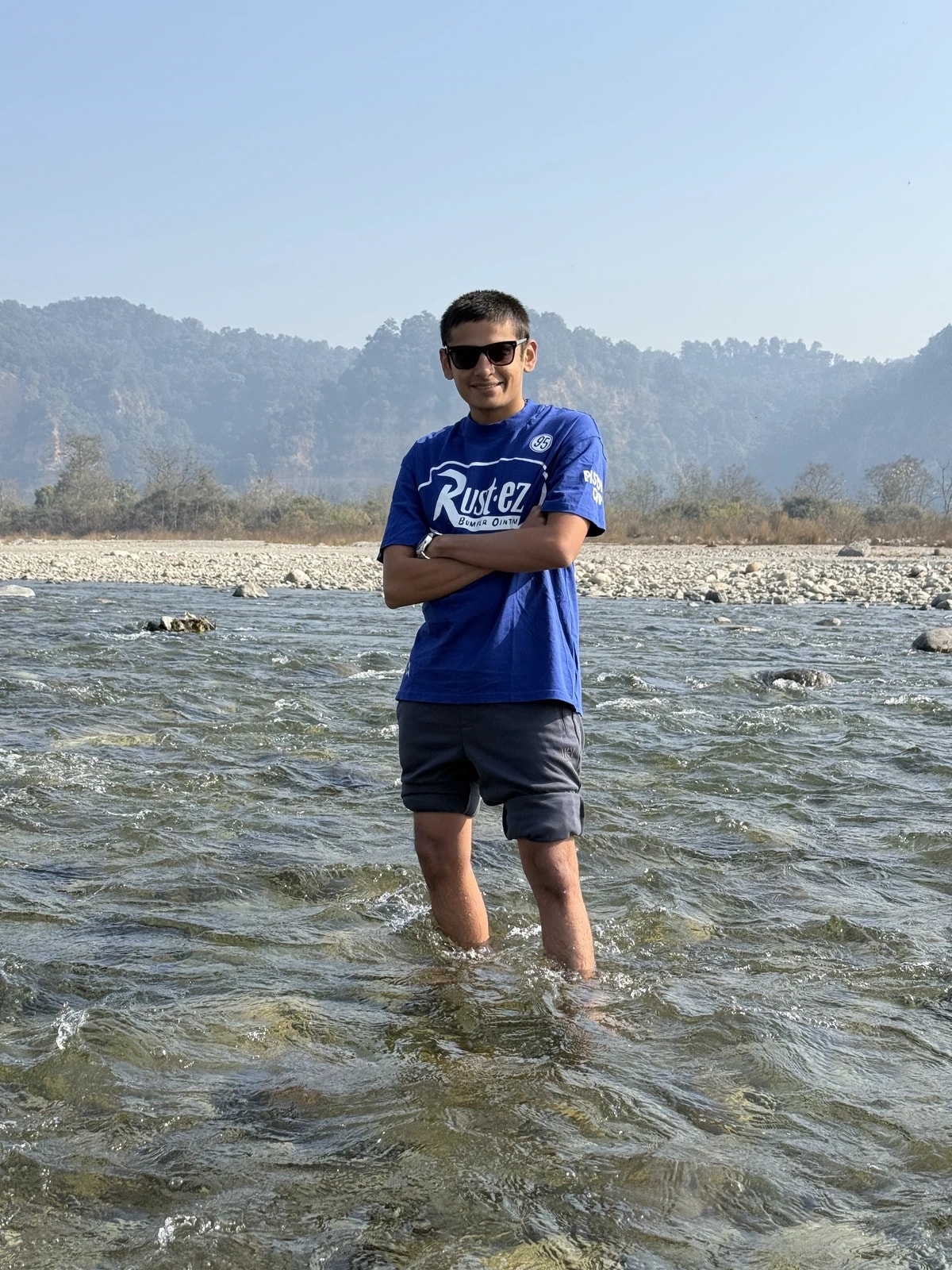 Tarang standing in a river with wooded hills behind him